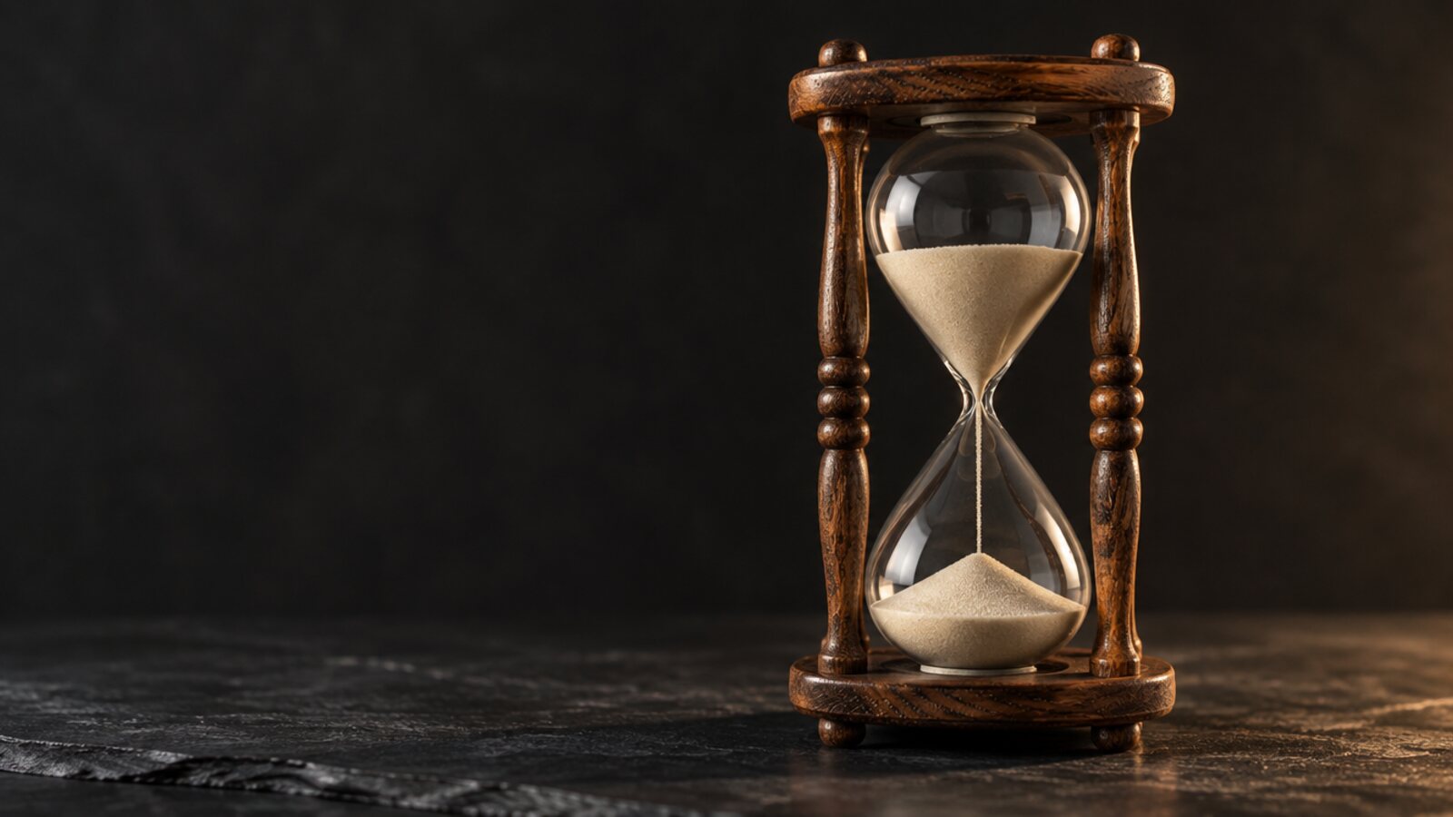 An hourglass on a dark surface, sand running through the neck